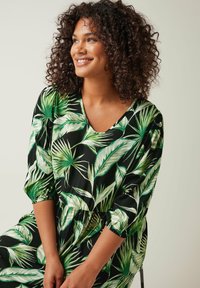 Zwarte jurk met een levendige groene bladerenprint, 3/4 mouwen met gerimpelde manchetten en een V-hals ontwerp. Lichtgewicht stof met een gladde textuur.