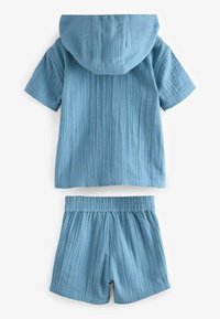 Lys blå børnetøj bestående af en kortærmet hættebluse og matchende shorts. Stoffet har et struktureret, krøllet mønster.