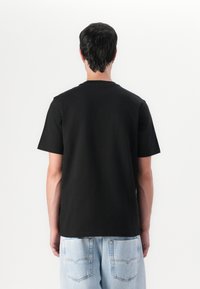 Svart bomull t-skjorte med korte ermer, rund hals og et enkelt design. Brukt med lys blå denimjeans med baklommer.