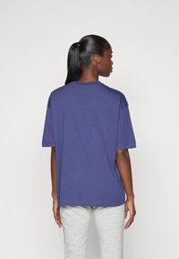 T-shirt blu navy a maniche corte realizzato in tessuto morbido, con una vestibilità comoda e scollo rotondo. Visto da dietro con pantaloni grigi.