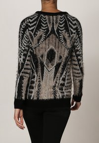 Maglione fuzzy nero e beige con motivi geometrici, texture lavorata a maglia e polsini e bordo inferiori a costine neri. Visualizzazione dalla parte posteriore.