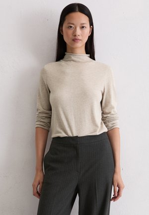 Beżowy sweter z golfem wykonany z miękkiego materiału, z długimi rękawami i luźnym fasonem, w połączeniu z ciemnymi spodniami w prążki.
