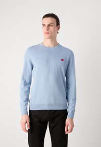 Hellblaues Sweatshirt aus weichem Strickstoff, mit Rundhalsausschnitt und kleinem roten Logo auf der linken Brust. Strukturierte Bündchen und Saum.