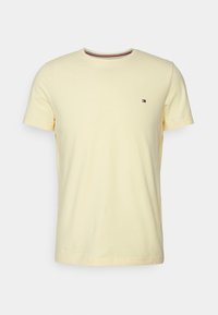 Vaaleankeltainen t-paita pehmeästä puuvillasta, jossa on lyhyet hihat ja pyöreä pääntie raidallisella sisäkauluksella. Pieni logo vasemmassa rinnassa.