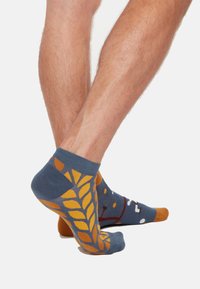 Sokken met een blauwe basis, gele bladerenpatronen en bruine accenten. Het design bevat een speelse illustratie met witte stippen.