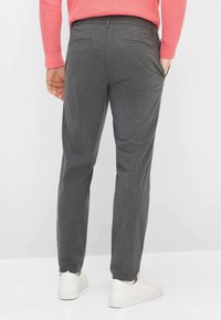 Grijze op maat gemaakte broek met een vlakke voorkant, schuine zijzakken en een slanke pasvorm. Draagt een roze trui en witte sneakers.