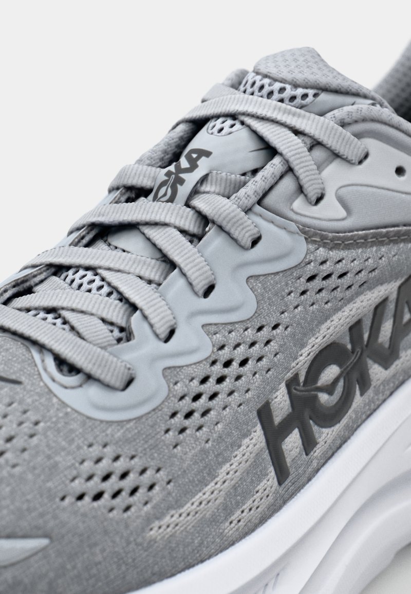 Gray running shoe featuring a breathable mesh upper, textured laces, and prominent brand logo on the side. White sole with subtle design accents.