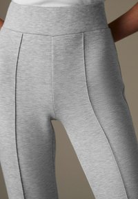 Helle graue Leggings mit hohem Bund und vertikalen Nahtdetails, gefertigt aus einem weichen, dehnbaren Stoff mit glatter Textur.