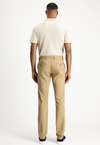 Khaki trousers with a straight cut, paired with a light beige polo shirt. Features buttoned back pockets and a smooth texture.