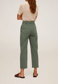 Groene katoenbroek met een hoge taille en taps toelopende benen. Gaat gepaard met een licht, textuur gebreid top, dat de achterzakken en naden toont.