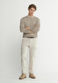 Beige långärmad skjorta med rund halsringning, i kombination med ljusbeige cargobyxor. En brun bälte och ljusbruna sneakers fulländar looken.