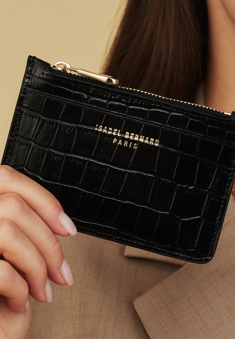 Portefeuille en cuir noir embossé crocodile avec quincaillerie dorée, doté d'une fermeture éclair et d'un logo embossé sur le devant. Design compact et rectangulaire.