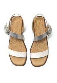 Sandalias de cuero con plantilla de un tono marrón claro, correas de cuero blancas y una hebilla plateada texturizada en la correa del tobillo. Diseño de suela plana.