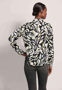 Langarmshirt, zwart-wit abstract patroon met gele accenten, lichte stof, klassieke kraag en een getailleerde pasvorm.
