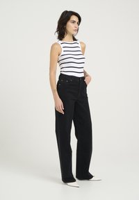 Vit tanktopp med svarta ränder, kombinerad med högmidjade svarta jeans. Jeansarna har rak benstil och diskret fickdetalj.