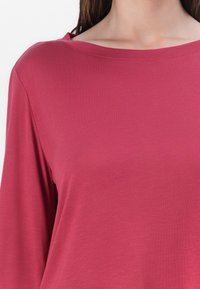Top aderent într-o culoare roz bogată, cu un decolteu larg și mâneci lungi. Fabricat dintr-un material moale, texturat.