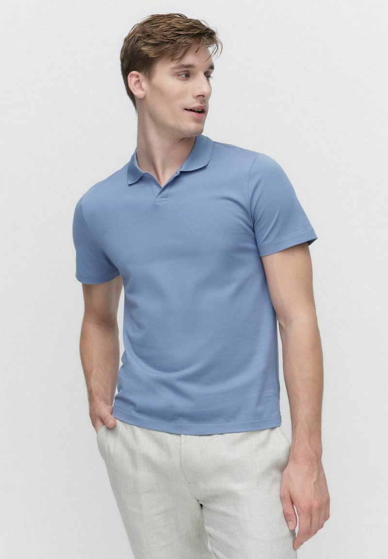 Ljusblå pikétröja i slät tyg, med klassisk krage och korta ärmar, tillsammans med ljusa linbyxor.