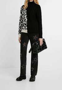 Pull en tricot torsadé noir et blanc avec imprimé animal, associé à un jean noir orné d'accents étoilés et à une pochette noire brillante.