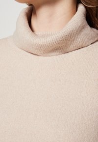 Jasnonudziasty sweter z golfem, wykonany z miękkiego, prążkowanego materiału. Posiada złożony kołnierz oraz gładką fakturę.