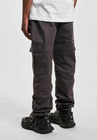 Pantalones cargo grises con múltiples bolsillos laterales, corte holgado y una tela duradera. Combinados con zapatillas deportivas negras con superficies texturizadas.