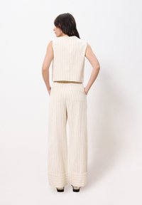 Cream-colored, sleeveless crop top with vertical pinstripes, paired with wide-leg pants featuring a matching waistband and cuffs.