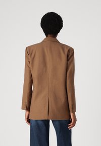 Brun skreddersydd blazer med en strukturert design, med slagkrager og enkel split bak. Har knappede mansjetter og en jevn tekstur.