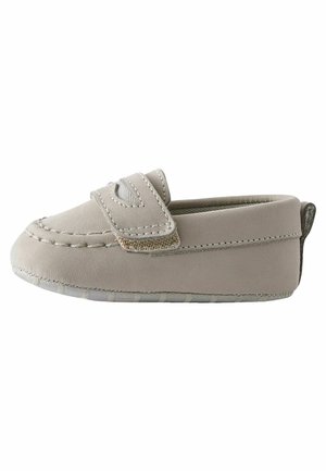Mocassin bébé beige avec un bout arrondi cousu, une large bride sur le dessus et une semelle en caoutchouc souple.