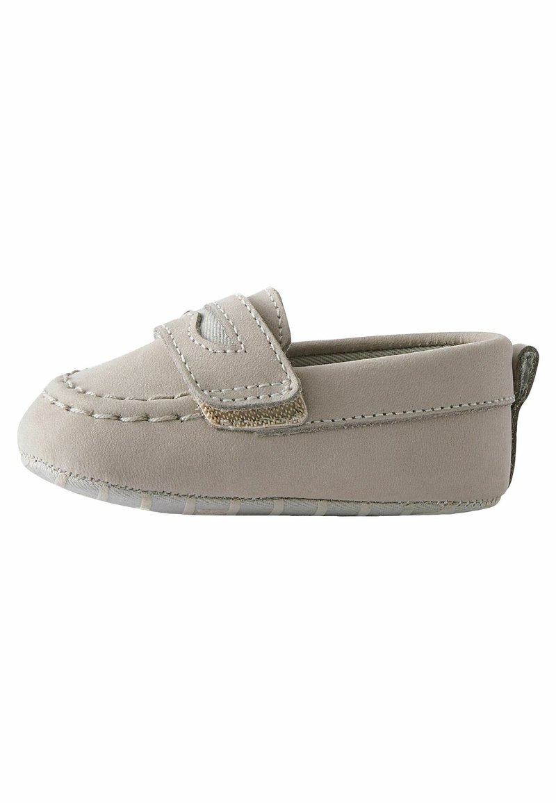 Mocassin bébé beige avec un bout arrondi cousu, une large bride sur le dessus et une semelle en caoutchouc souple.