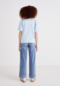 T-shirt azzurro chiaro con maniche a sbuffo arricciate, abbinato a jeans in denim chiaro a gamba larga con orlo sfrangiato e calzature casual.
