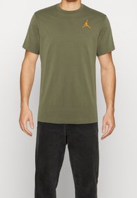 Olive green short-sleeve T-shirt made of cotton, featuring a small orange Jumpman logo on the left chest. Classic crew neck design.