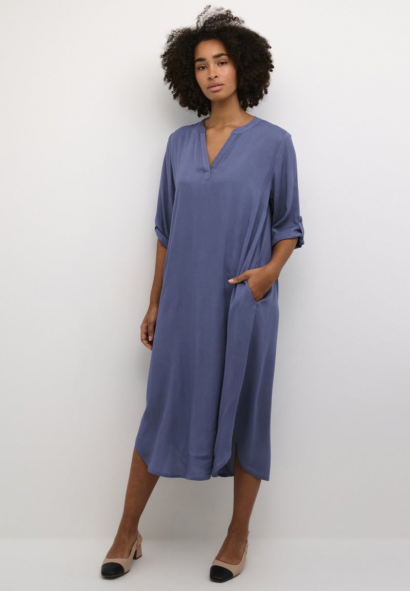 Robe légère bleu profond avec un col en V, des manches trois-quarts et des poches sur les côtés. Texture lisse et design mi-long avec des fentes latérales.