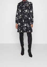 Musta mekko, jossa on valkoinen tähtikuosi, röyhelökaulus ja pitkät hihat, yhdistettynä kimalteleviin mustiin reiteen asti ulottuviin saappaisiin.