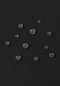 Wassertropfen, die auf einem schwarzen strukturierten Stoff perlend liegen und die wasserabweisenden oder wasserdichten Materialeigenschaften veranschaulichen.