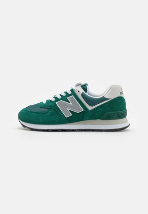 Baskets New Balance vertes et blanches en suède et mesh, lacets blancs, logo gris et semelle rembourrée sur fond uni.