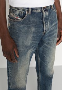 Siniset farkut haalistuneella pesulla, kevyellä kulutuksella, viiden taskun mallilla ja näkyvällä merkkilapulla takataskussa.