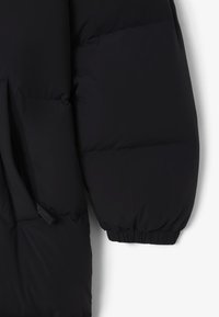 Chaqueta acolchada negra con acabado mate. Presenta un diseño acolchado grande, puños elásticos y un bolsillo lateral con apertura oculta.