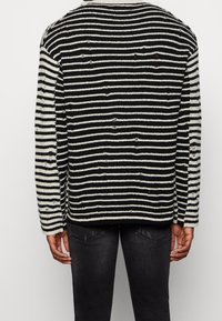 Czarnobiały sweter w paski wykonany z teksturowanej tkaniny, o luźnym kroju z wykończeniem z postrzępionymi detalami i okrągłym dekoltem.