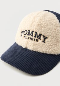 Tumed sinine korgsamatööri müts kreemikate sherpa fliispaneelidega ja musta tikandiga "Tommy Hilfiger" esipaneelil.