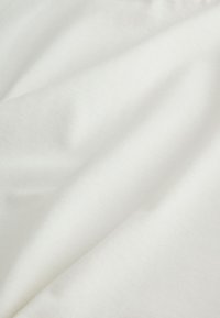 Gros plan sur un tissu blanc lisse présentant des plis doux et une texture fine à la lumière naturelle.