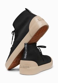 Ζευγάρι μαύρα πλεκτά υψηλά sneakers με μπεζ σόλες, καφέ υφασμάτινα πατούμενα και "OMBRE" επώνυμα λουράκια έλξης στη φτέρνα και στη σόλα.