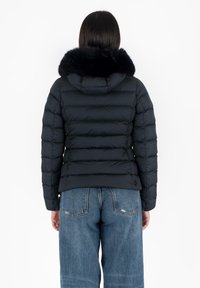 Giacca a vento nera con cappuccio, dotata di colletto in pelliccia sintetica, design trapuntato e dettagli con bottoni, abbinata a jeans a gamba larga blu chiaro.