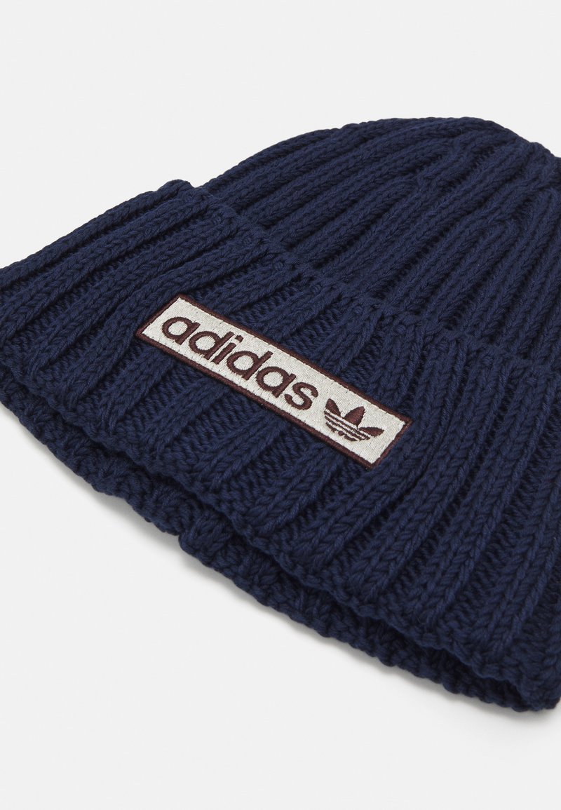 Granatowa dziana czapka z prążkowanym wzorem, z prostokątną białą naszywką z logo "adidas" oraz godłem w kolorze bordowym.
