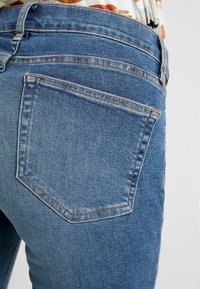 Blå denimjeans med en klassisk bakfickdesign, med kontrasterande sömmar och midjhöjd. Slät textur och passform.