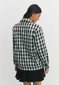 Cămașă flanelată în carouri alb-negru, cu mâneci lungi, manșete cu nasturi și guler. Are croială dreaptă și textură subtilă.