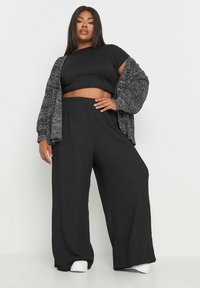 Svart kort topp, texturerad grå cardigan och vida svarta byxor. Outfiten har en lös passform och elastisk midja.