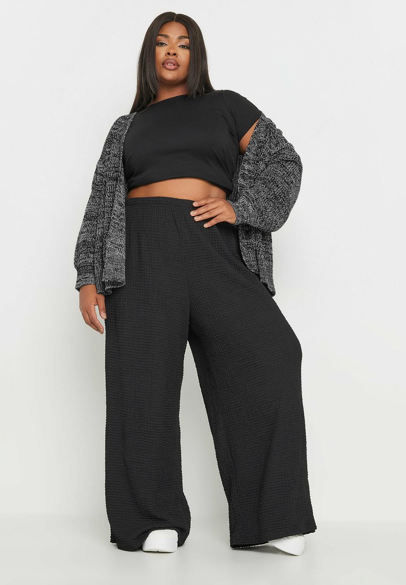 Svart kort topp, texturerad grå cardigan och vida svarta byxor. Outfiten har en lös passform och elastisk midja.