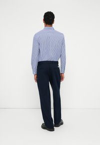 Gaiši zils un balts svītrots garām piedurknēm krekls ar klasisku apkakli, apvienots ar tumši ziliem pielāgotiem biksēm un melnām kurpēm. Aizmugures skats.