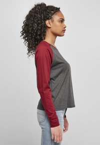 Graues und burgunderfarbenes Langarmshirt mit rundem Ausschnitt und kontrastierenden Ärmeln, aus einem weichen, strukturierten Stoff. Seitenansicht.