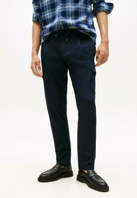 Pantaloni cargo blu navy con vita regolabile, tasche laterali e vestibilità slim. Tessuto liscio e leggero, abbinati a mocassini neri.