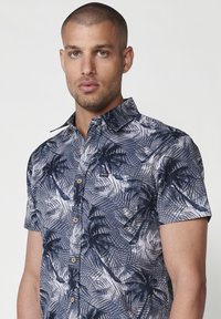 Camisa de manga corta en azul marino con un patrón de hojas de palma, con diseño de botones y cuello, hecha de tejido ligero.